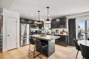 Kitchen featuring a kitchen bar, stainless steel appliances, dark stone countertops, a center island, and hanging light fixtures