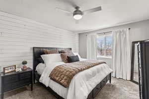 Carpeted bedroom with wood walls, a ceiling fan, and a textured ceiling