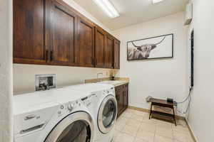 Washroom with cabinet space, washer and clothes dryer, and light tile patterned floors