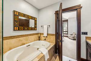 Bathroom with a tub with jets, vanity, and light carpet