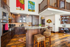 Kitchen featuring dark wood-style floors, a kitchen breakfast bar, a high ceiling, appliances with stainless steel finishes, and glass insert cabinets
