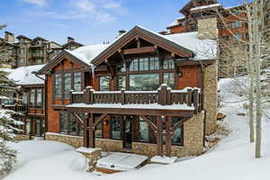 Snow covered rear of property with a chimney, stone siding, and a patio