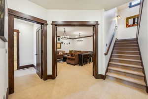 Corridor with light carpet, crown molding, stairway, and a chandelier