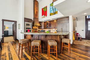 Kitchen featuring dark wood-type flooring, a breakfast bar, recessed lighting, stainless steel appliances, and glass insert cabinets