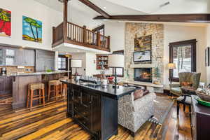 Living area featuring dark wood-style flooring, a stone fireplace, beamed ceiling, and high vaulted ceiling