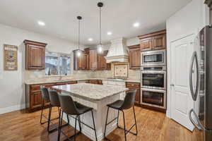 Kitchen with light stone countertops, appliances with stainless steel finishes, backsplash, pendant lighting, and a kitchen bar