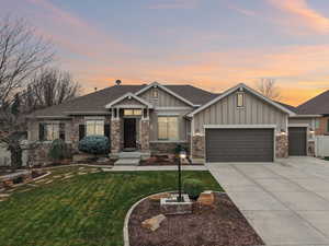 Craftsman house featuring board and batten siding, a shingled roof, a lawn, concrete driveway, and stone siding
