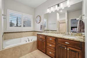 Ensuite bathroom featuring double vanity, a bath, and light tile patterned floors