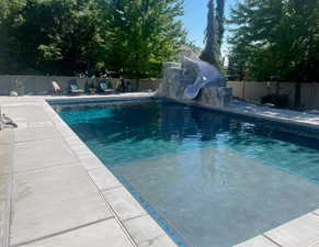Summertime View of swimming pool with a fenced backyard, a water slide, and a patio area