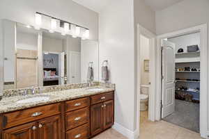 Ensuite bathroom with double vanity, a walk in closet, and light tile patterned floors