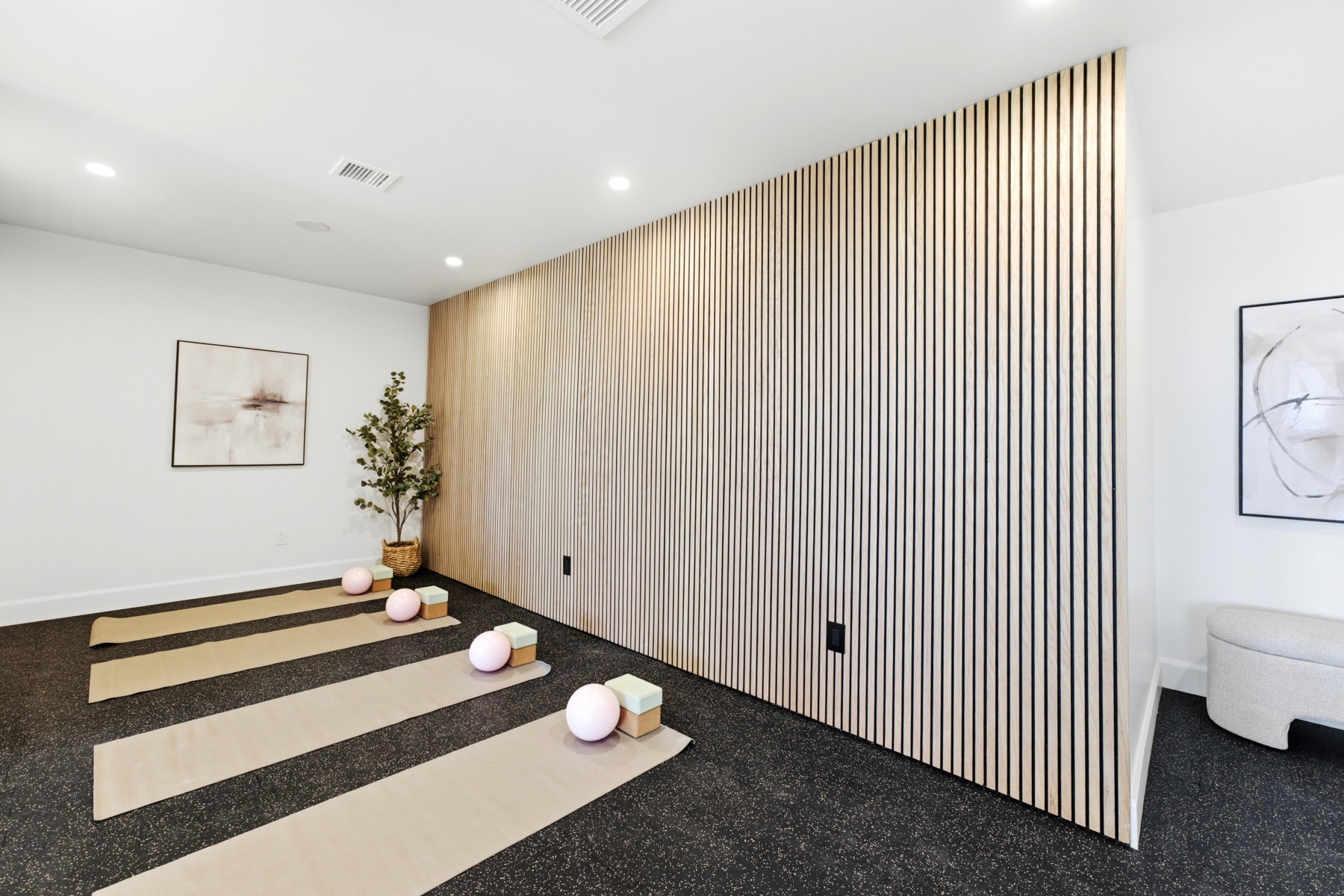 Recessed lighting illuminates a versatile room featuring a full wall with vertical slat wood-finish paneling