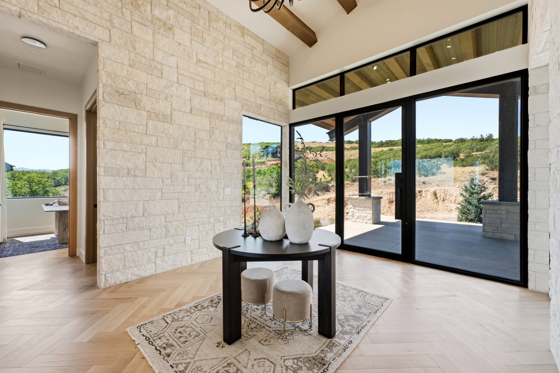 Grand entry featuring a stone accent wall, herringbone wood-finish flooring, vaulted ceiling with exposed beam, and expansive glass doors opening to a covered patio