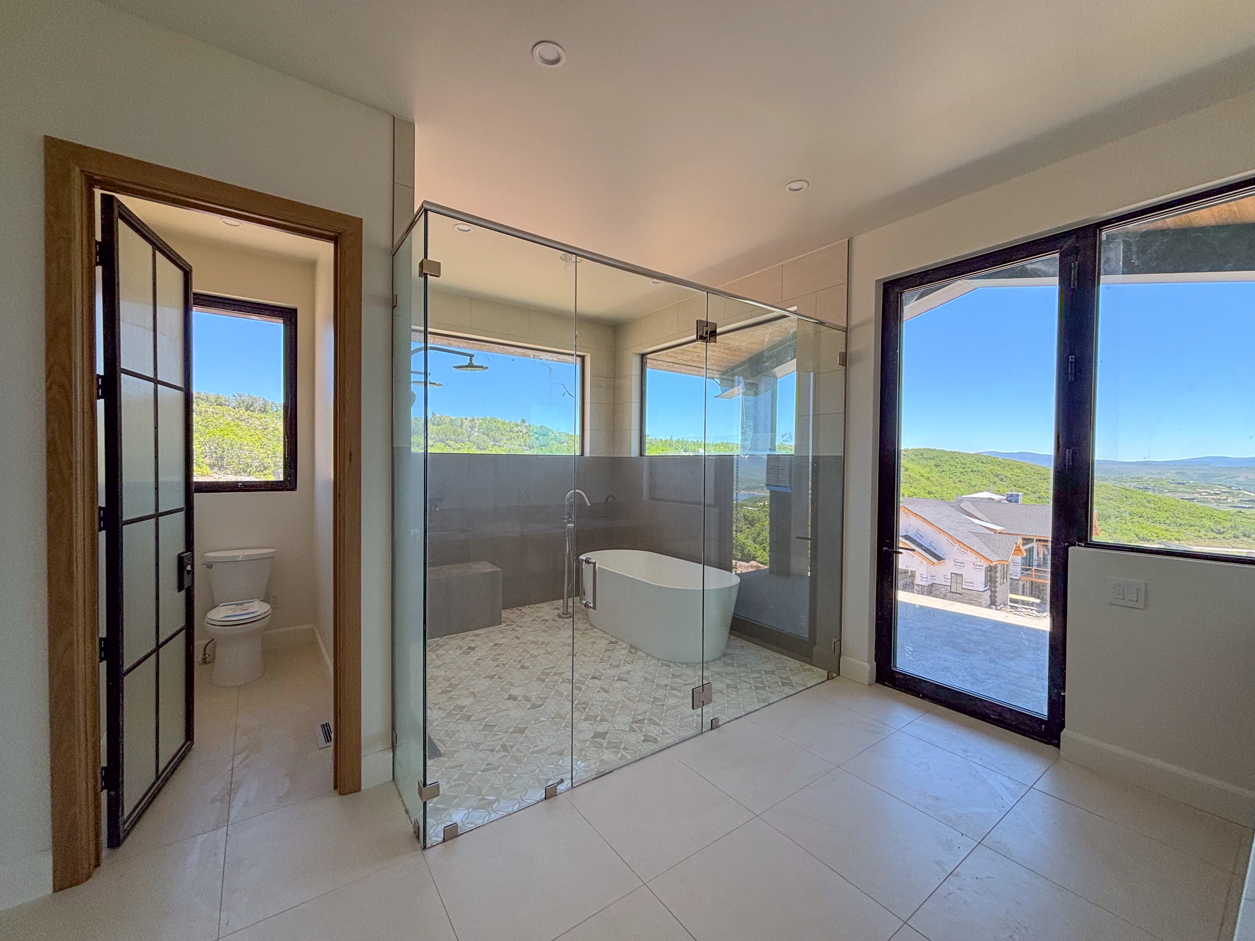 Spacious bathroom featuring a frameless glass shower enclosure with a built-in bench, a freestanding soaking tub, and large format floor tiling