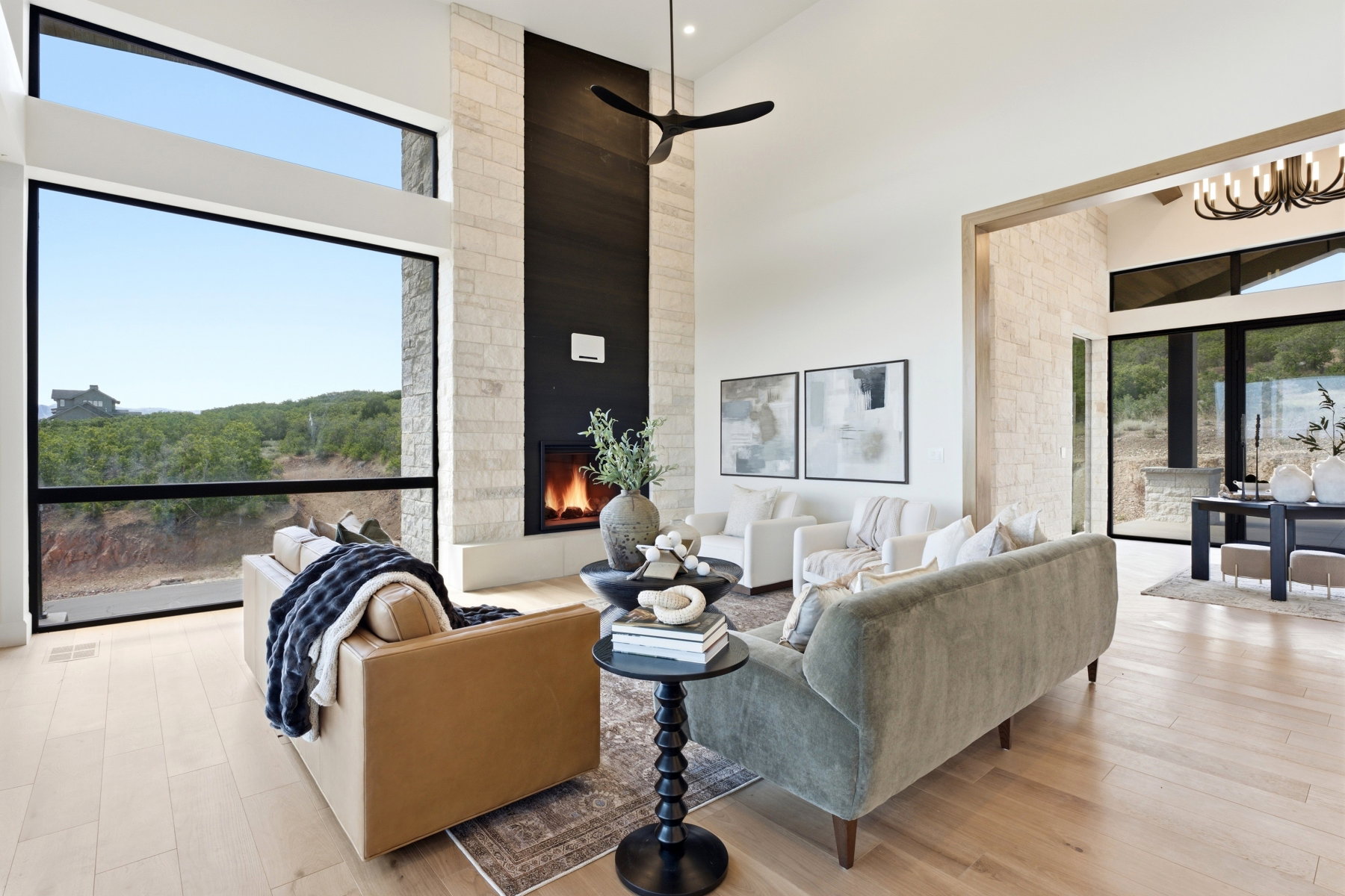 Spacious open-concept living area featuring a floor-to-ceiling stone fireplace, expansive windows, wood-finish flooring, and high ceilings