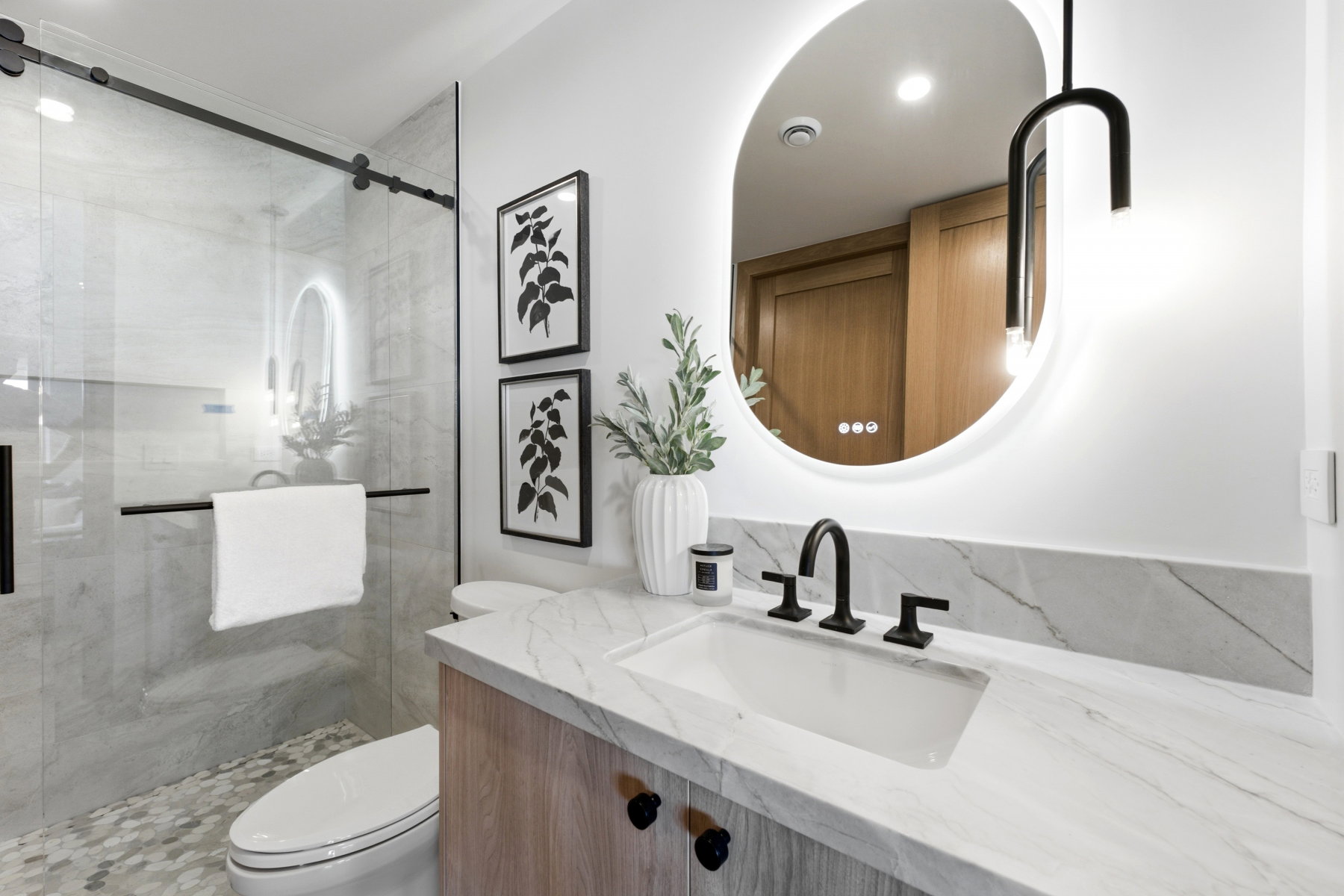 Bathroom featuring a walk-in shower with glass enclosure, a vanity with a white countertop and integrated sink, a back-lit oval mirror, and a wood-finish vanity cabinet