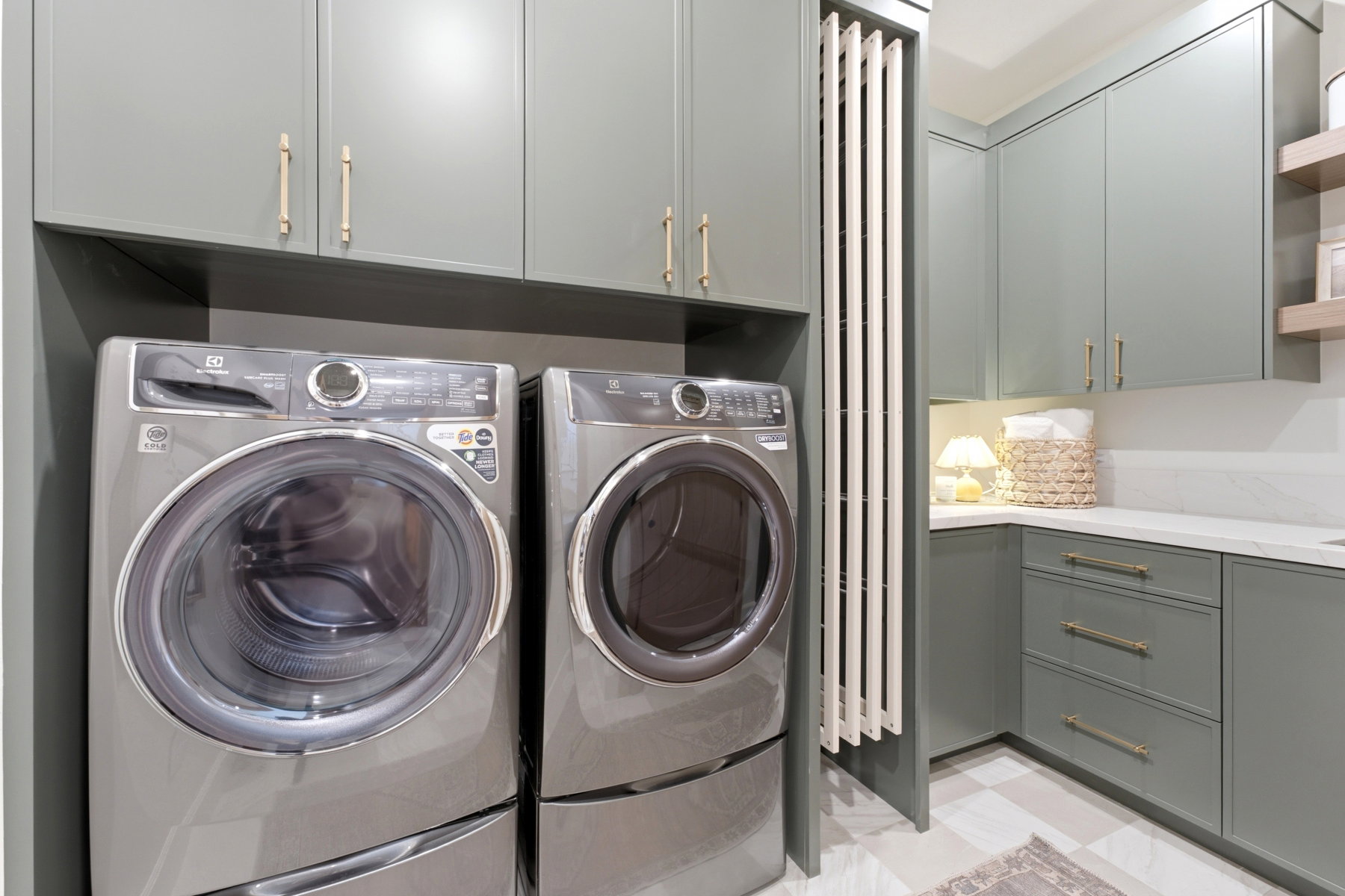 Laundry area featuring sleek grey cabinetry with gold-toned hardware, a built-in folding rack, and a white countertop