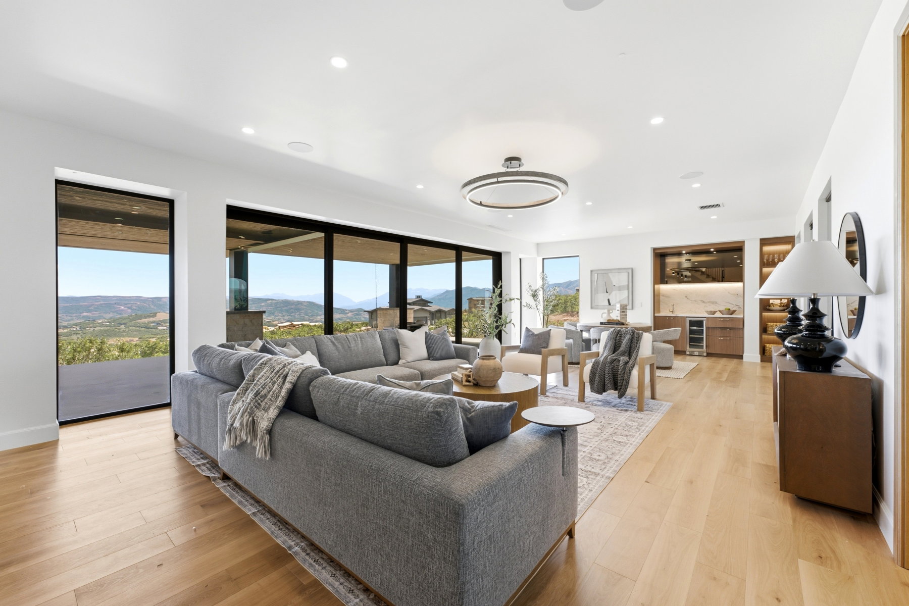 Open-concept living area featuring expansive glass sliding doors, wood-finish flooring, a built-in wet bar with a wine refrigerator, and recessed lighting