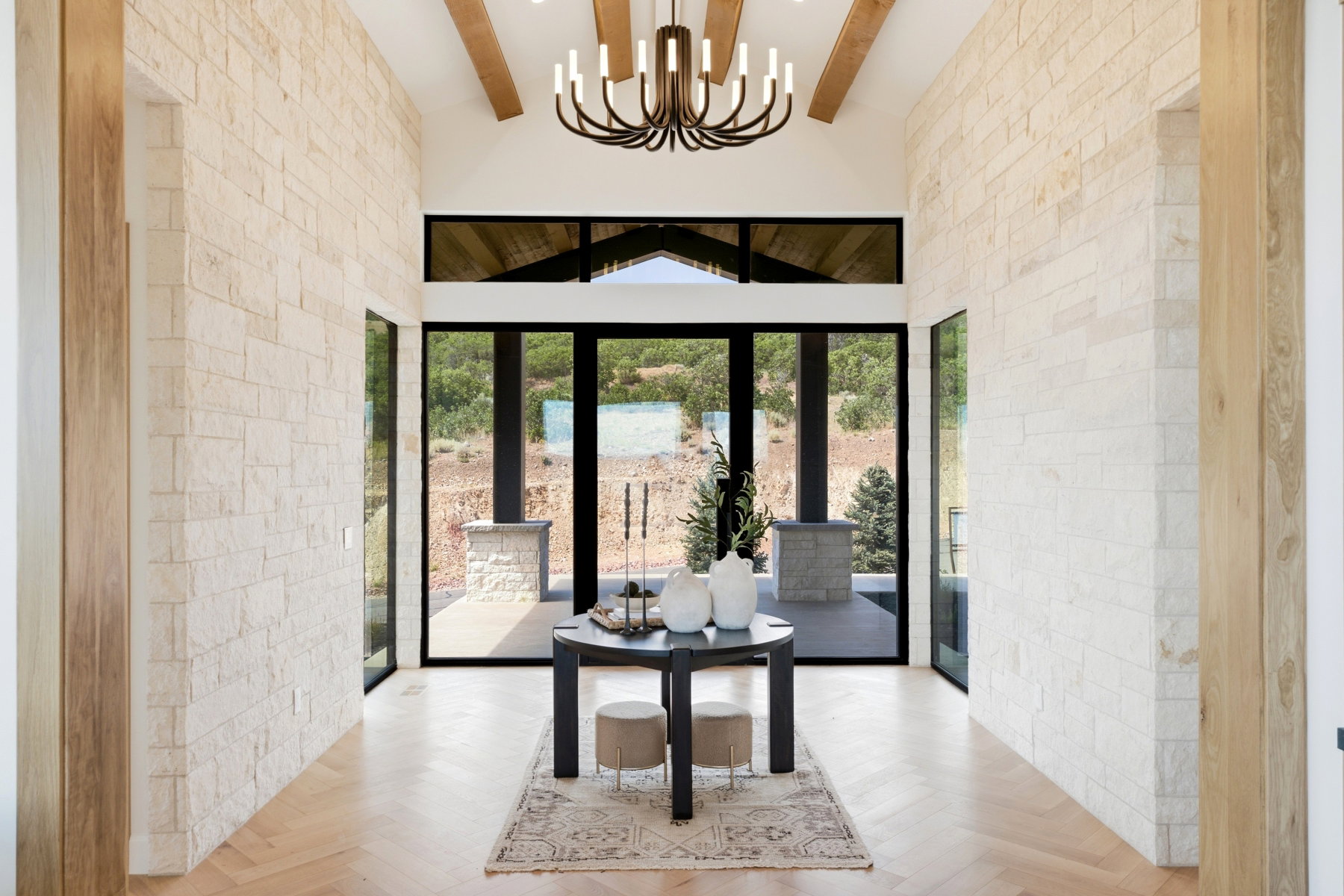 Entryway featuring light-toned stacked stone walls, wood-finish herringbone flooring, and a vaulted ceiling with exposed wood beams