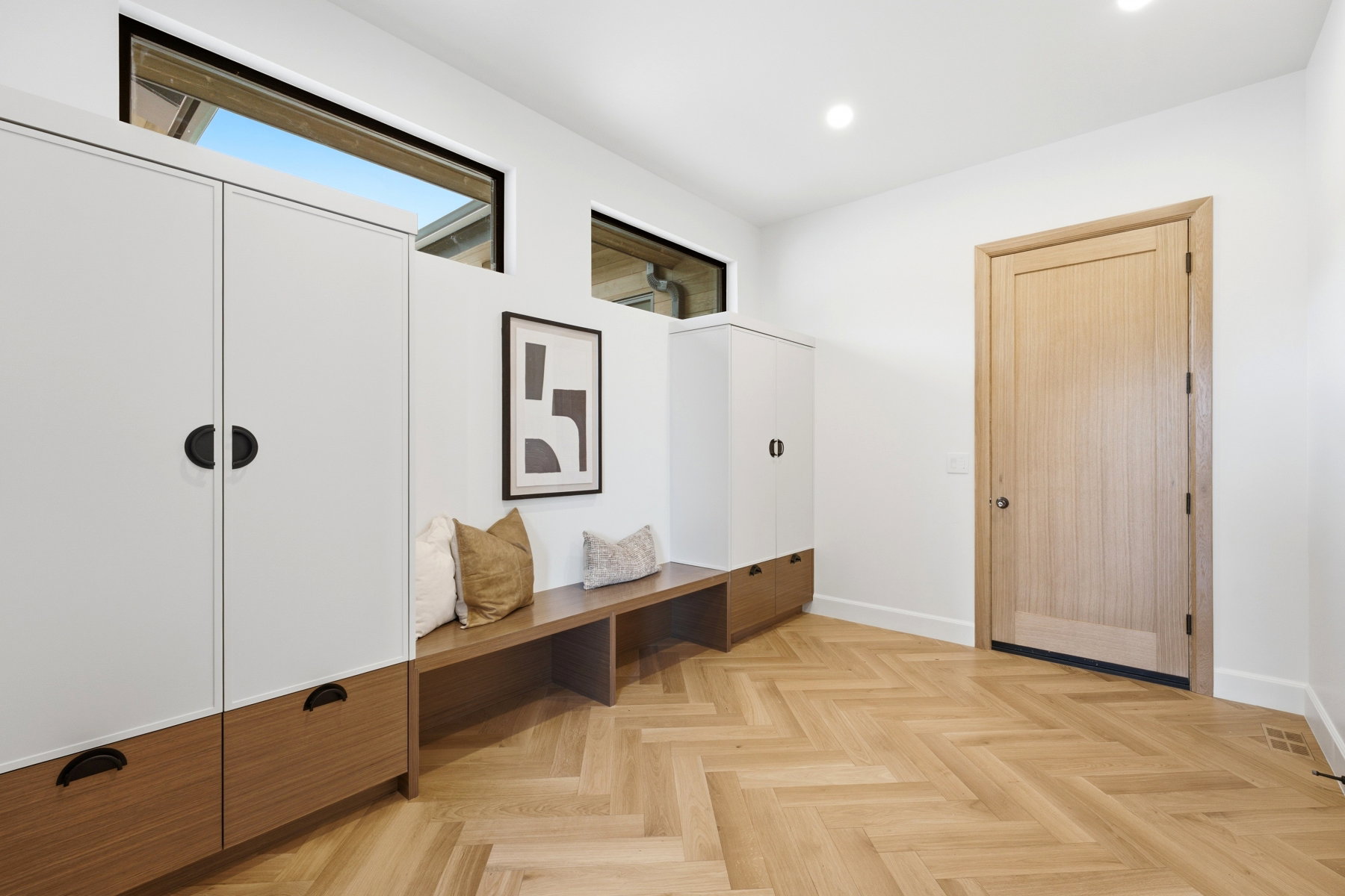 Entryway featuring herringbone wood-finish flooring, integrated white and wood-finish cabinetry, a built-in wood bench, and transom windows