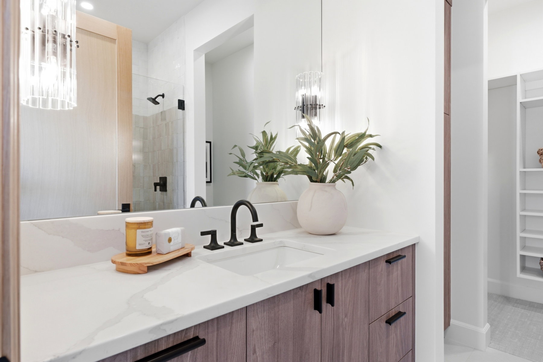 Bathroom vanity featuring a light-toned wood-finish cabinetry, quartz-style countertop, and matte black fixtures
