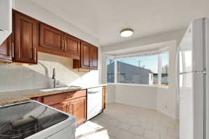 Kitchen with electric range, freestanding refrigerator, light stone countertops, stainless steel dishwasher, and backsplash