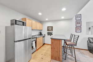 Kitchen with appliances with stainless steel finishes, a kitchen bar, light brown cabinetry, a peninsula, and dark countertops