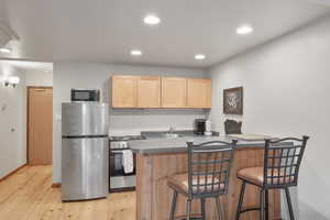 Kitchen featuring light brown cabinets, stainless steel appliances, light wood-style floors, recessed lighting, and a breakfast bar