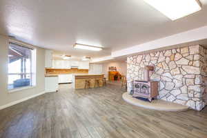 Kitchen with a wood stove, light countertops, wood finish floors, white cabinets, and a textured ceiling