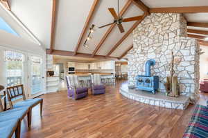 Living room featuring a wood stove, high vaulted ceiling, ceiling fan, light wood-style floors, and beamed ceiling
