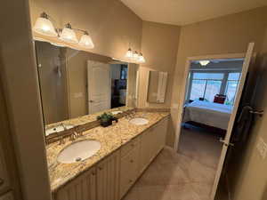 Ensuite bathroom featuring double vanity, light tile patterned flooring, light colored carpet, and a shower