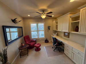 Home office with built in desk, ceiling fan, light colored carpet, , plantation shutters, and recessed lighting
