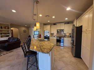 Kitchen with a kitchen breakfast bar, appliances with stainless steel finishes, decorative light fixtures, light stone countertops, and open floor plan