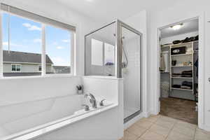 Full bath featuring a walk in closet, a stall shower, a garden tub, light tile patterned floors, and light carpet