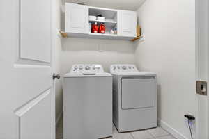 Washroom featuring washing machine and clothes dryer, light tile patterned floors, and cabinet space
