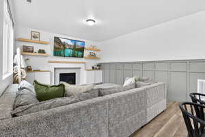 Living area featuring a decorative wall, light wood-style flooring, a tiled fireplace, and a wainscoted wall