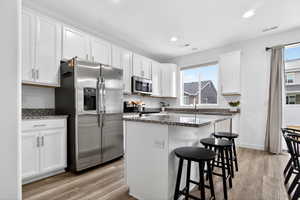 Kitchen with a breakfast bar area, stainless steel appliances, dark stone counters, white cabinetry, and light wood-style floors