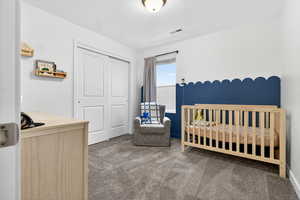 Bedroom featuring a nursery area, dark carpet, and a closet