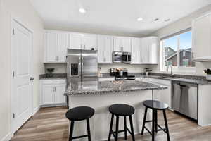 Kitchen with a breakfast bar area, white cabinetry, appliances with stainless steel finishes, dark stone countertops, and a center island