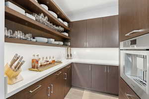 Bar area featuring stainless steel oven, modern cabinets, open shelves, light countertops, and dark brown cabinets