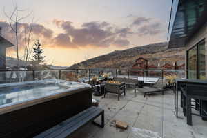 Patio terrace at dusk featuring a patio, a mountain view, a hot tub, and an outdoor living space with a fire pit