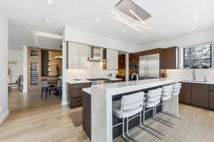 Kitchen featuring a breakfast bar, light stone countertops, modern cabinets, built in appliances, and wall chimney exhaust hood