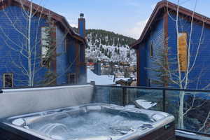 Snow covered property with a chimney, a hot tub, a balcony, and a mountain view