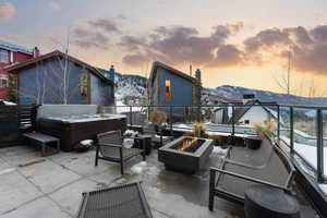 Patio terrace at dusk featuring a patio area, a hot tub, a mountain view, and an outdoor living space with a fire pit