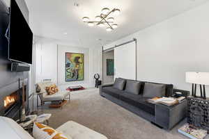Carpeted living room featuring a lit fireplace, a barn door, and a chandelier