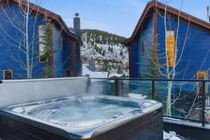 Snow covered patio with a mountain view, a hot tub, and a balcony