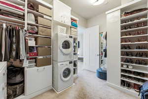 Laundry area featuring stacked washing machine and dryer and light colored carpet