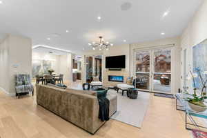 Living room featuring a chandelier, light wood finished floors, a glass covered fireplace, and recessed lighting