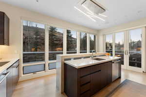 Kitchen with dark brown cabinetry, modern cabinets, light wood-style flooring, stainless steel dishwasher, and light stone counters