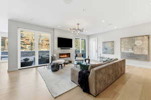 Living area featuring light wood-type flooring, a glass covered fireplace, a chandelier, and recessed lighting