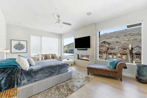 Bedroom featuring wood finished floors, a large fireplace, and ceiling fan